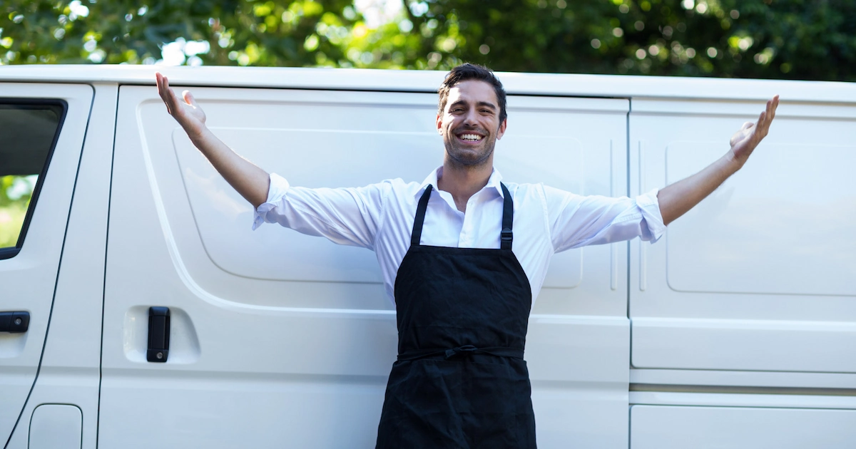 Un artisan menuisier sourit devant son camion professionnel affichant le nouveau logo de son entreprise.