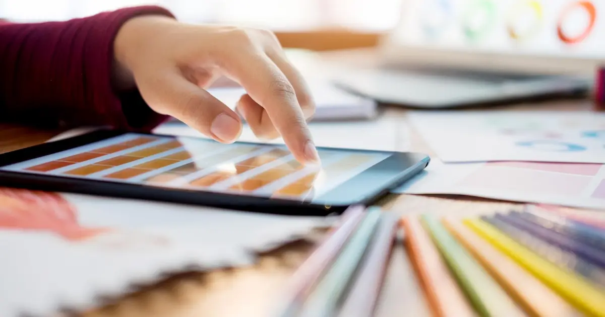 Une tablette affichant l'application Canva posée sur un bureau à côté d'une charte graphique imprimée au Mans